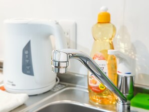 Een keukenkraan met een moderne kraan, een witte waterkoker en een fles afwasmiddel.