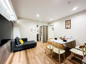 A modern living room with a sofa, a dining table with chairs, and a kitchen area with a refrigerator. - HANASTAY TSUMUGI (Osaka)