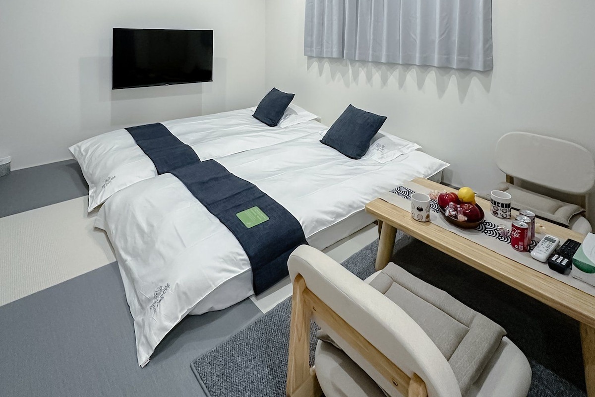 A modern hotel room with a large bed, a flat-screen TV, an air conditioning unit, and a small table with a chair.