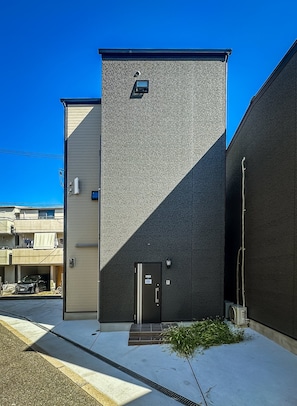 A building with a textured facade, a door, and a small window. - HANASTAY TSUMUGI (Osaka)
