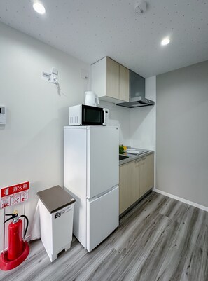 A compact kitchen with a microwave, stove, and a small trash bin. - HANASTAY TSUMUGI (Osaka)