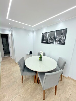 Un comedor moderno con una mesa redonda, sillas tapizadas en gris y una obra de arte con un motivo urbano en la pared.
