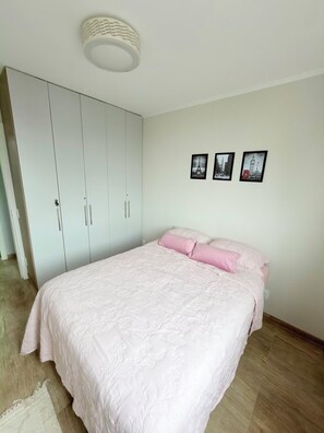 A bedroom with a bed, a wardrobe, and three framed pictures on the wall. - Feet in the sand via ferry (Rio de Janeiro)