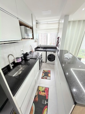 A compact kitchen with a sink, stove, and a washing machine. - Feet in the sand via ferry (Rio de Janeiro)