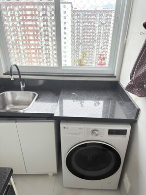 Cocina compacta con lavabo, lavadora y ventana con vistas a una zona residencial.