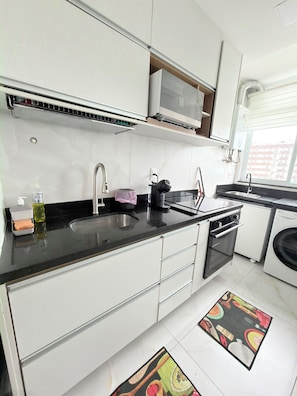 A modern kitchen with white cabinets, a black countertop, a stainless steel sink, and a microwave. - Feet in the sand via ferry (Rio de Janeiro)