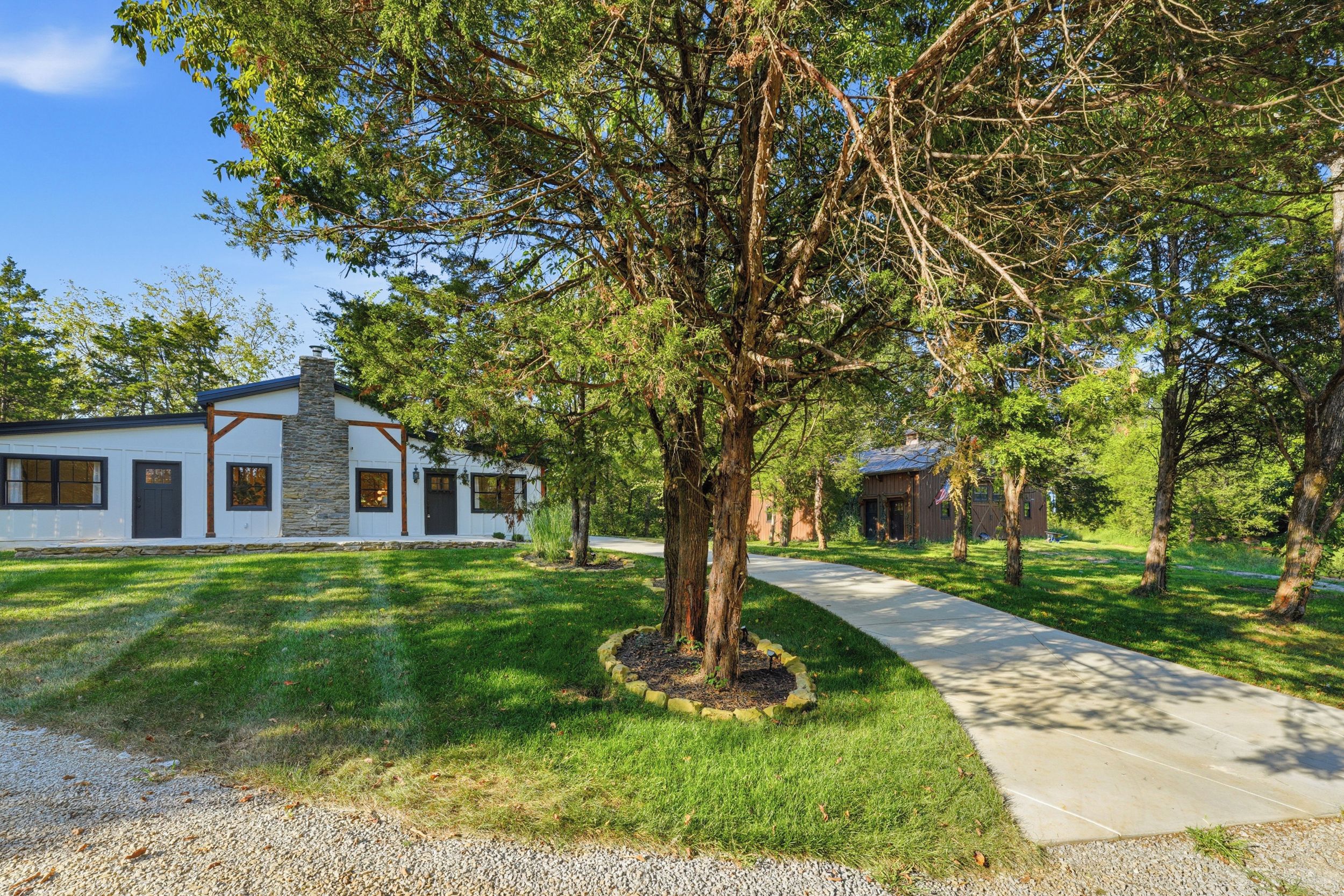 A residential property with a stone chimney, a well-maintained lawn, and a pathway leading to a wooden structure.