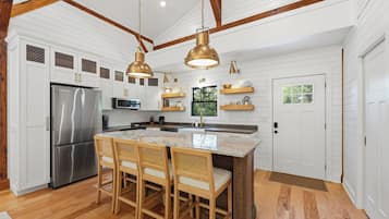 Une cuisine moderne avec un îlot central, des chaises en bois et des luminaires suspendus.