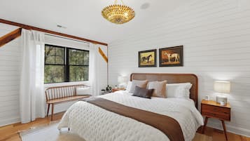 Une chambre à coucher avec un grand lit, un banc, une table de chevet, une lampe et deux tableaux encadrés accrochés au mur.