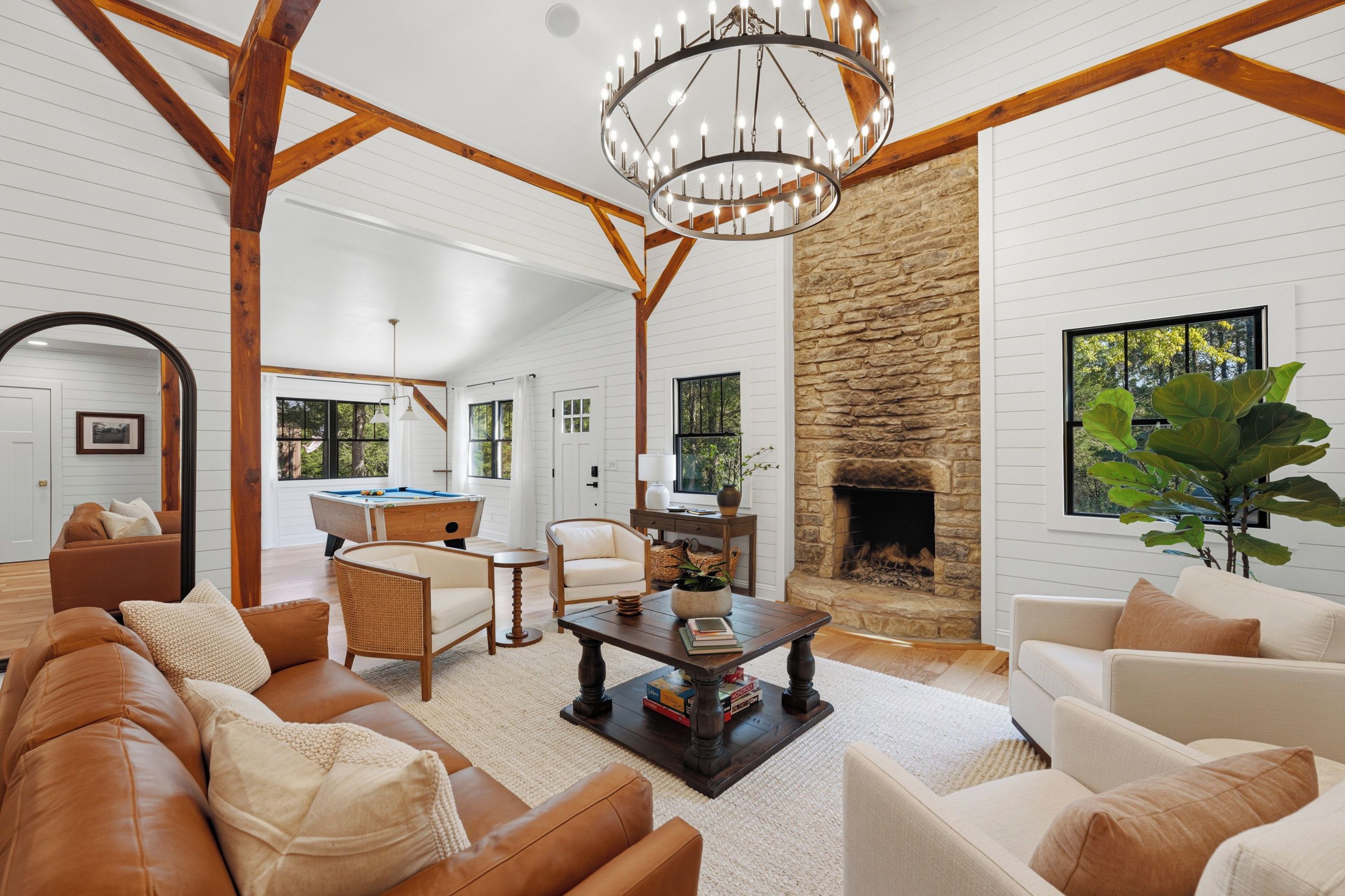 A spacious living room with a pool table, comfortable seating, a fireplace, and a large window with a view of greenery.