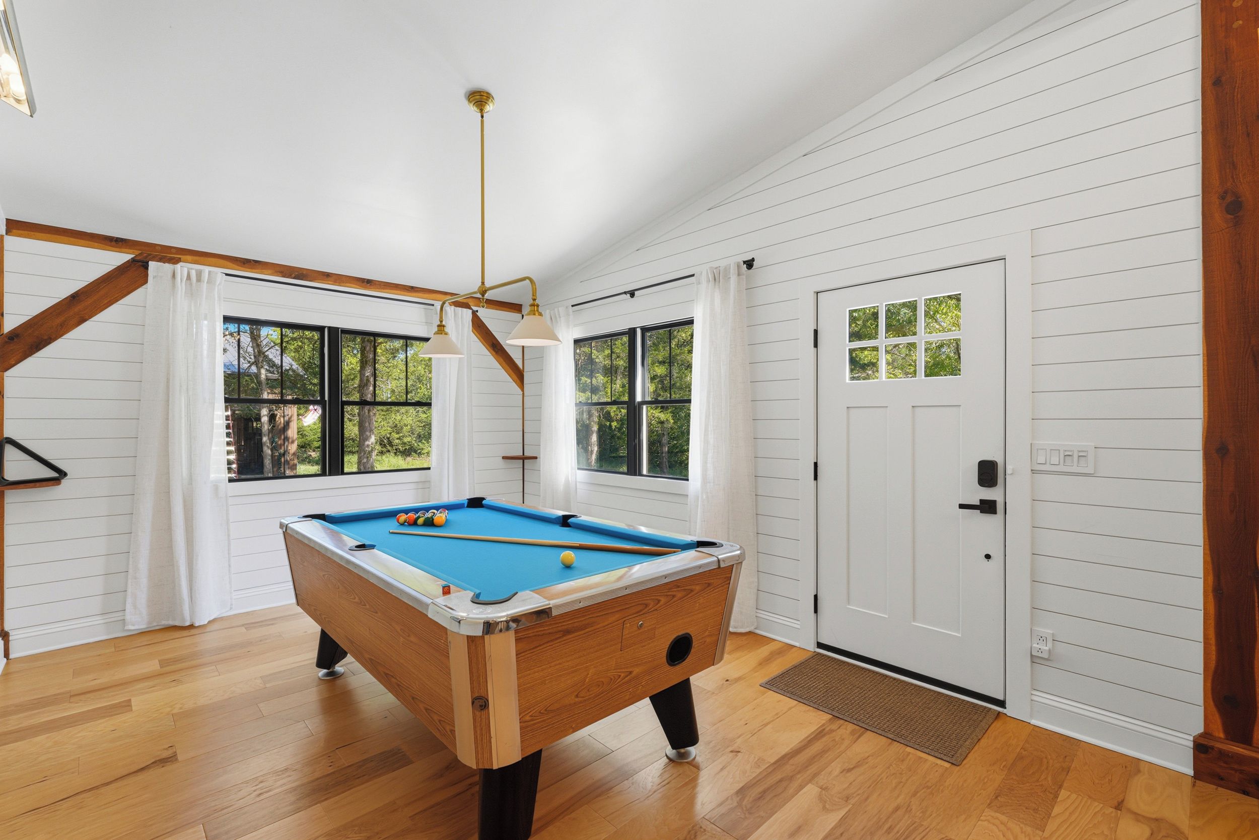 A pool table in a room with wooden floors, white walls, and a door with a window.