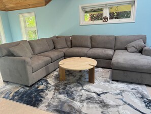 Ein Ecksofa mit rundem Couchtisch in einem Zimmer mit blauer Wand und Fenster.
