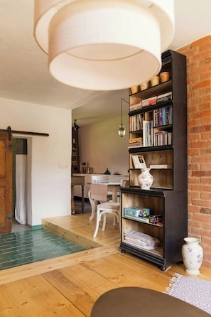 A cozy living room with a wooden floor, a bookshelf filled with books, a white vase, and a table with chairs.