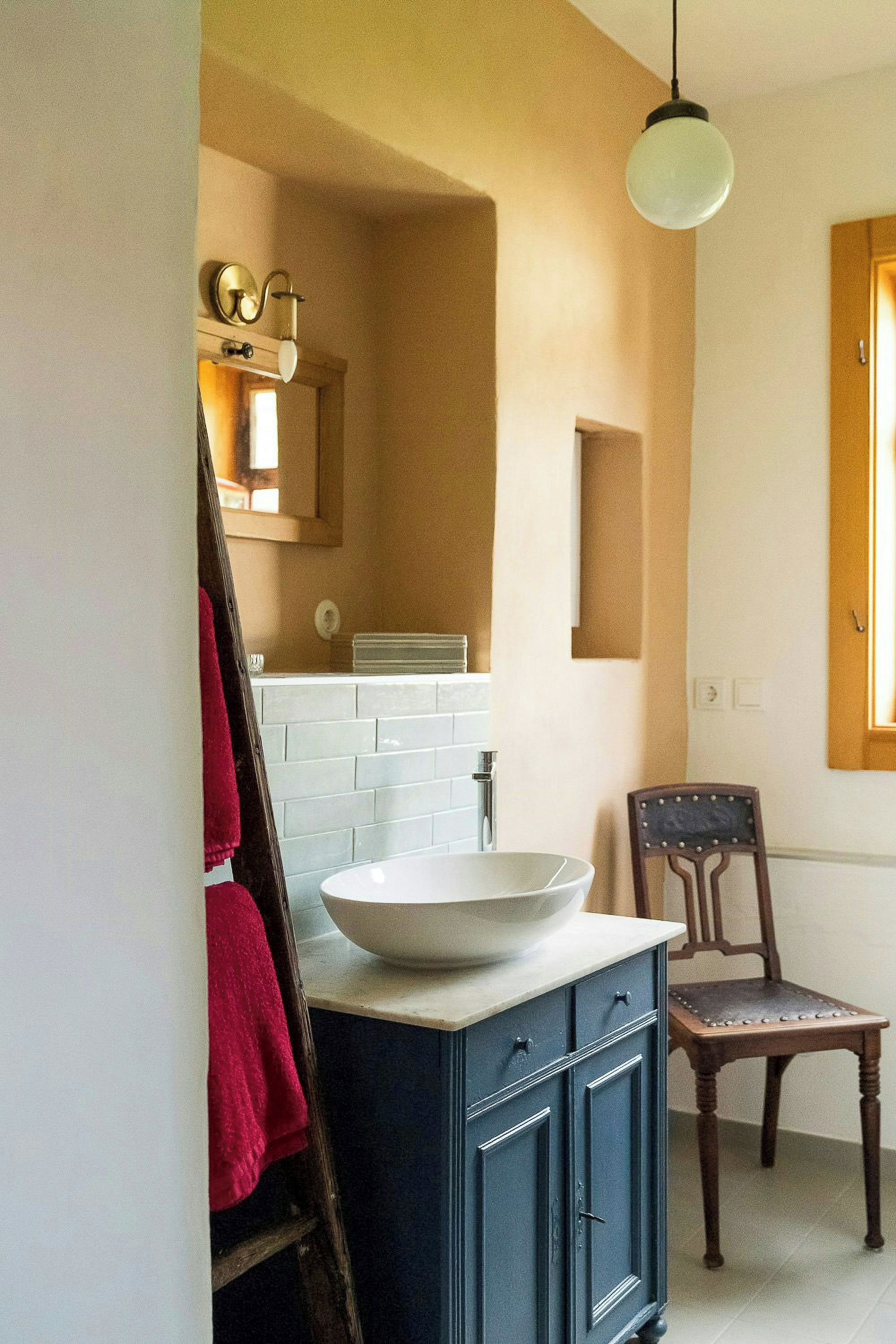 A bathroom with a white sink, a wooden chair, and a towel rack.