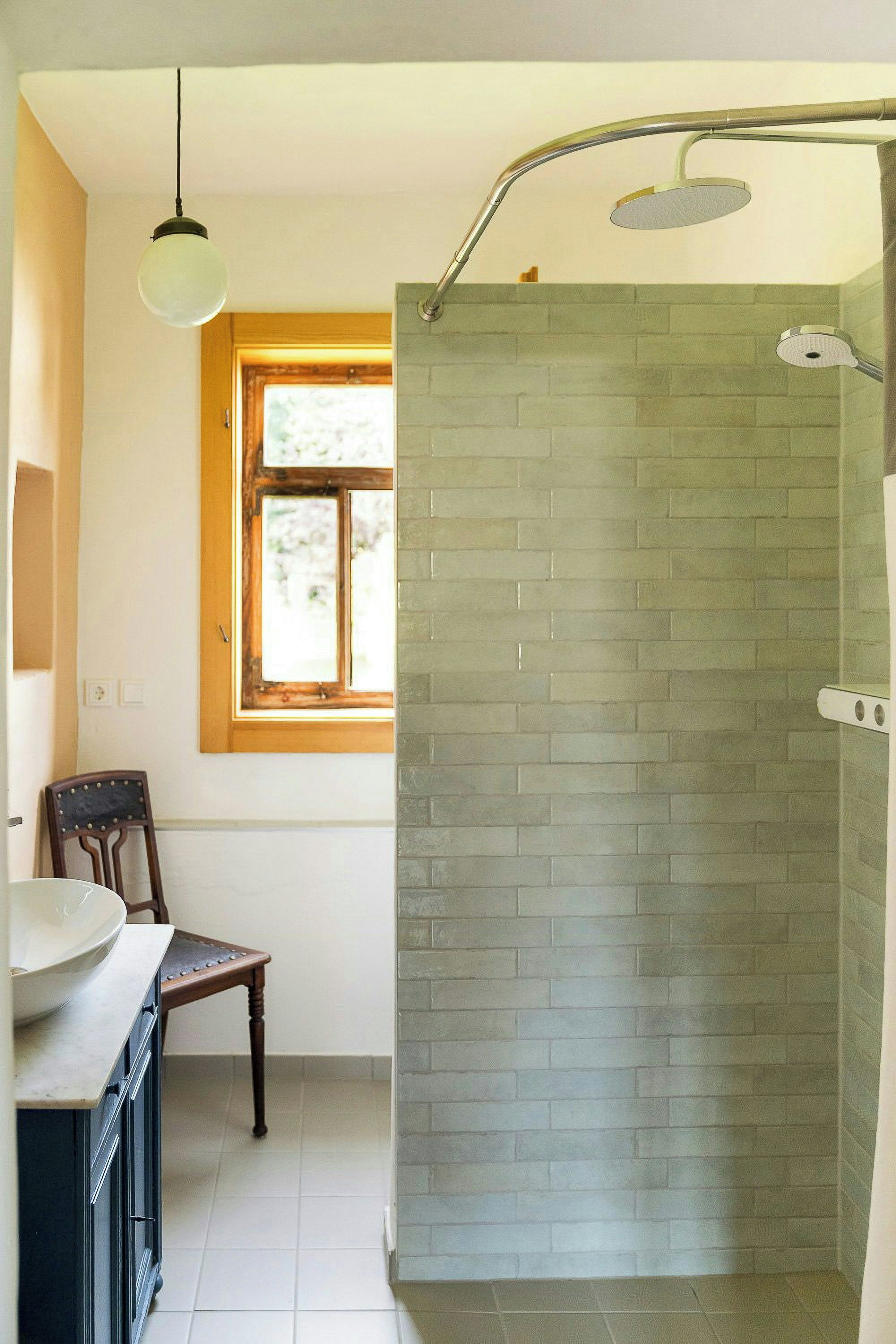 Ein Badezimmer mit Dusche, Waschbecken, einem Stuhl und einem Fenster.