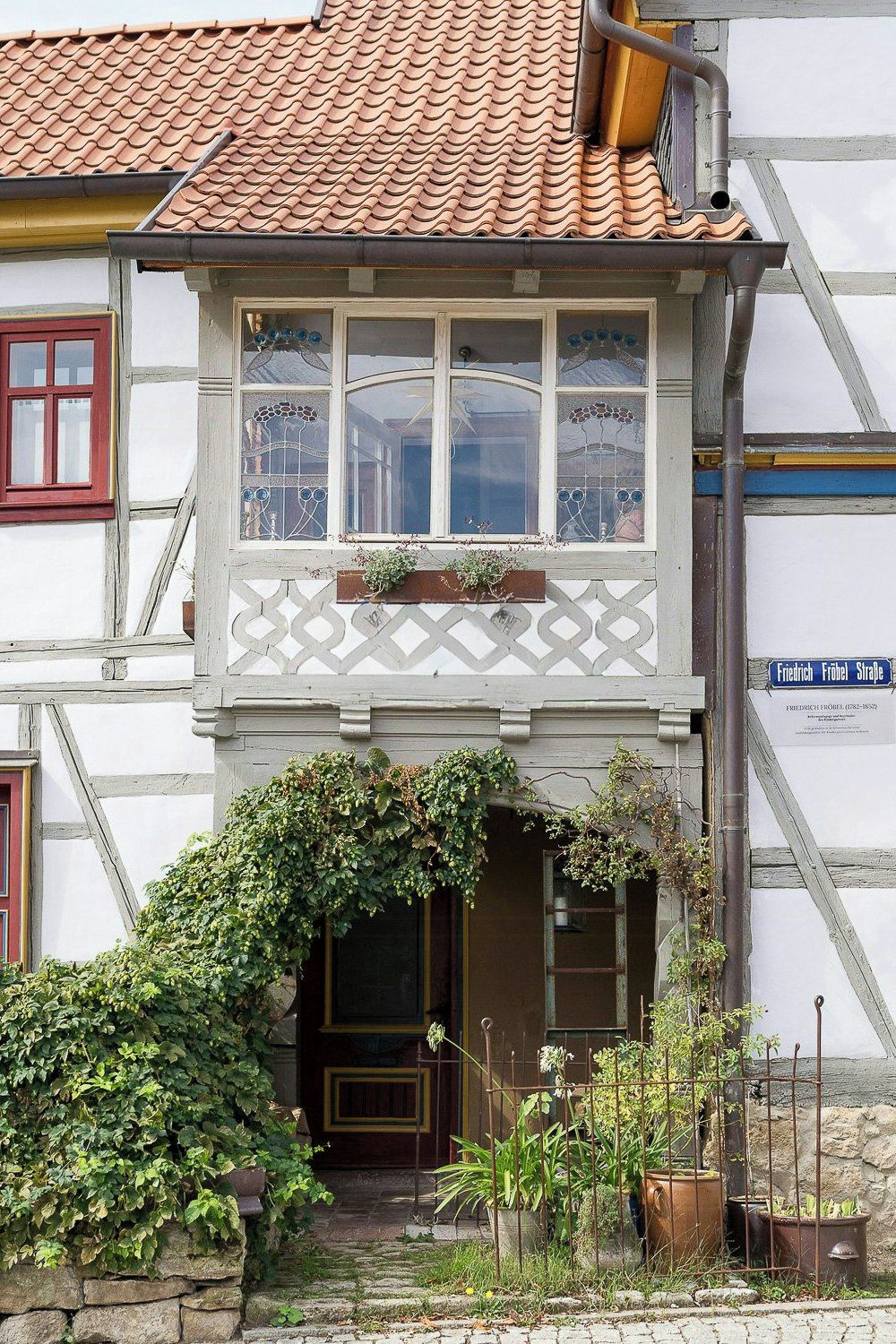A traditional half-timbered building with a dormer window, a stone entrance, and a sign indicating a historical site.