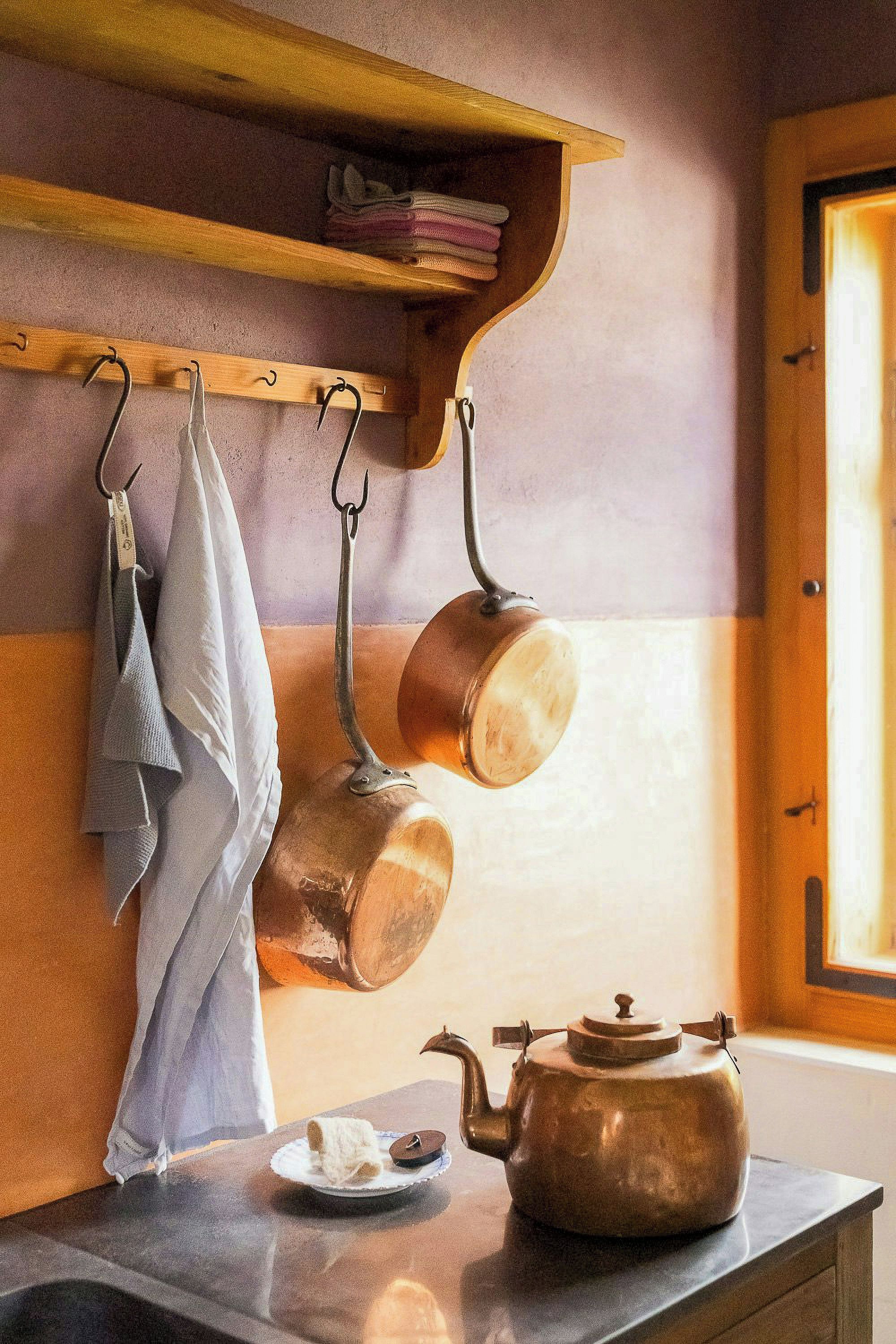 Et køkken med ophængte redskaber, en elkedel og en hylde med sammenfoldede håndklæder.