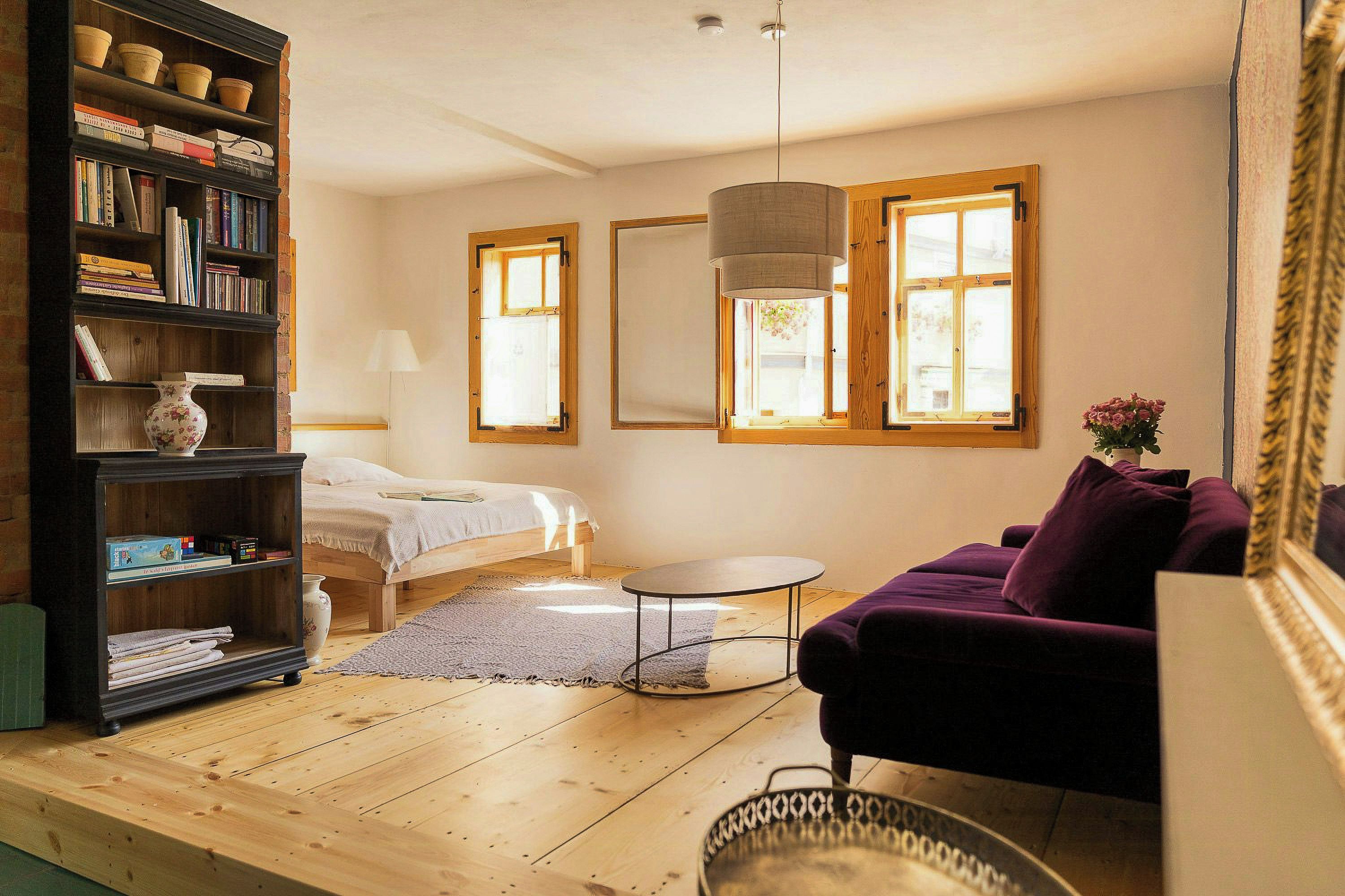 Una habitación acogedora con una cama, un sofá morado, una mesita redonda y una estantería llena de libros.