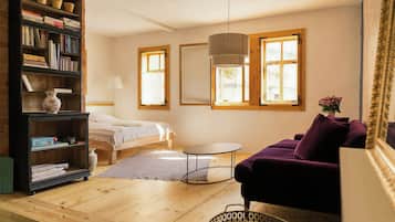 Una habitación acogedora con una cama, un sofá morado, una mesita redonda y una estantería llena de libros.