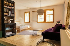 A cozy room with a bed, a purple sofa, a small round table, and a bookshelf filled with books.