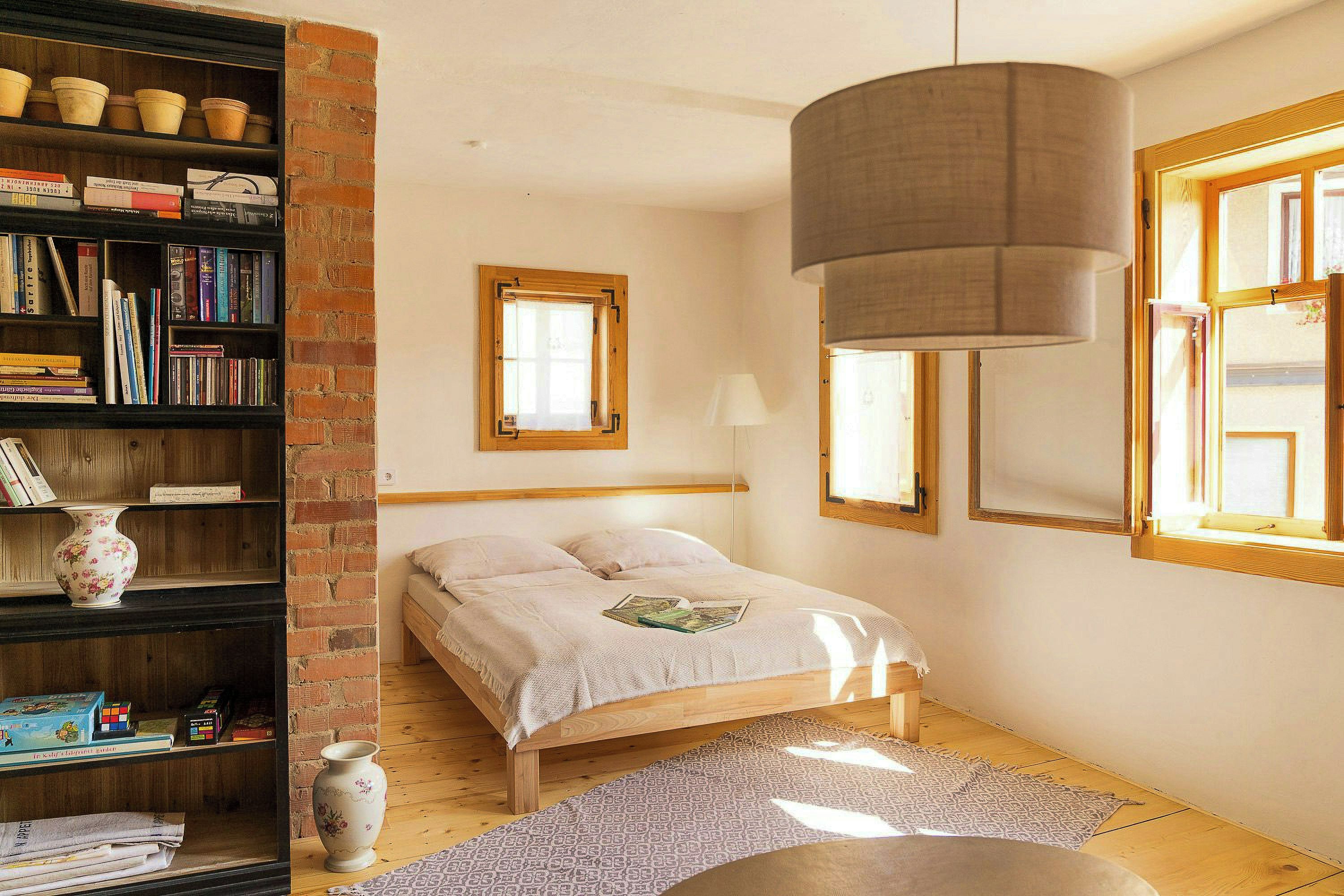 Ein Schlafzimmer mit einem Bett, einem Bücherregal, einem Fenster und einer Pendelleuchte.
