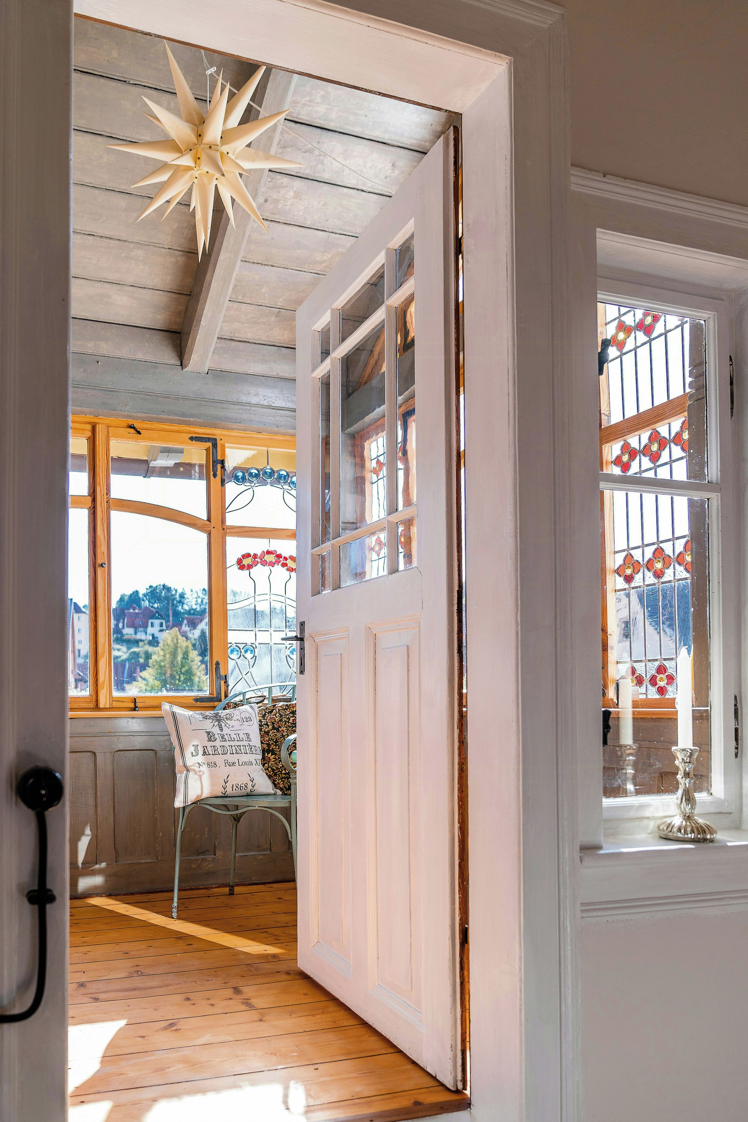 A room with a wooden floor, a white door, and a window with stained glass.