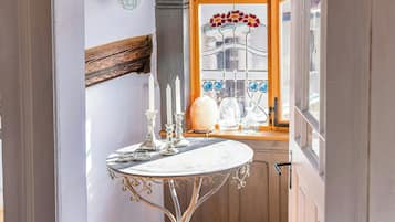 Un pasillo estrecho con una puerta blanca que da a una habitación con suelo de madera y una mesa con velas.