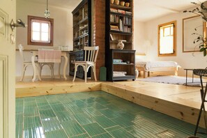 A room with a wooden floor, a bookshelf, a chair, a table with a cloth, and a bed.