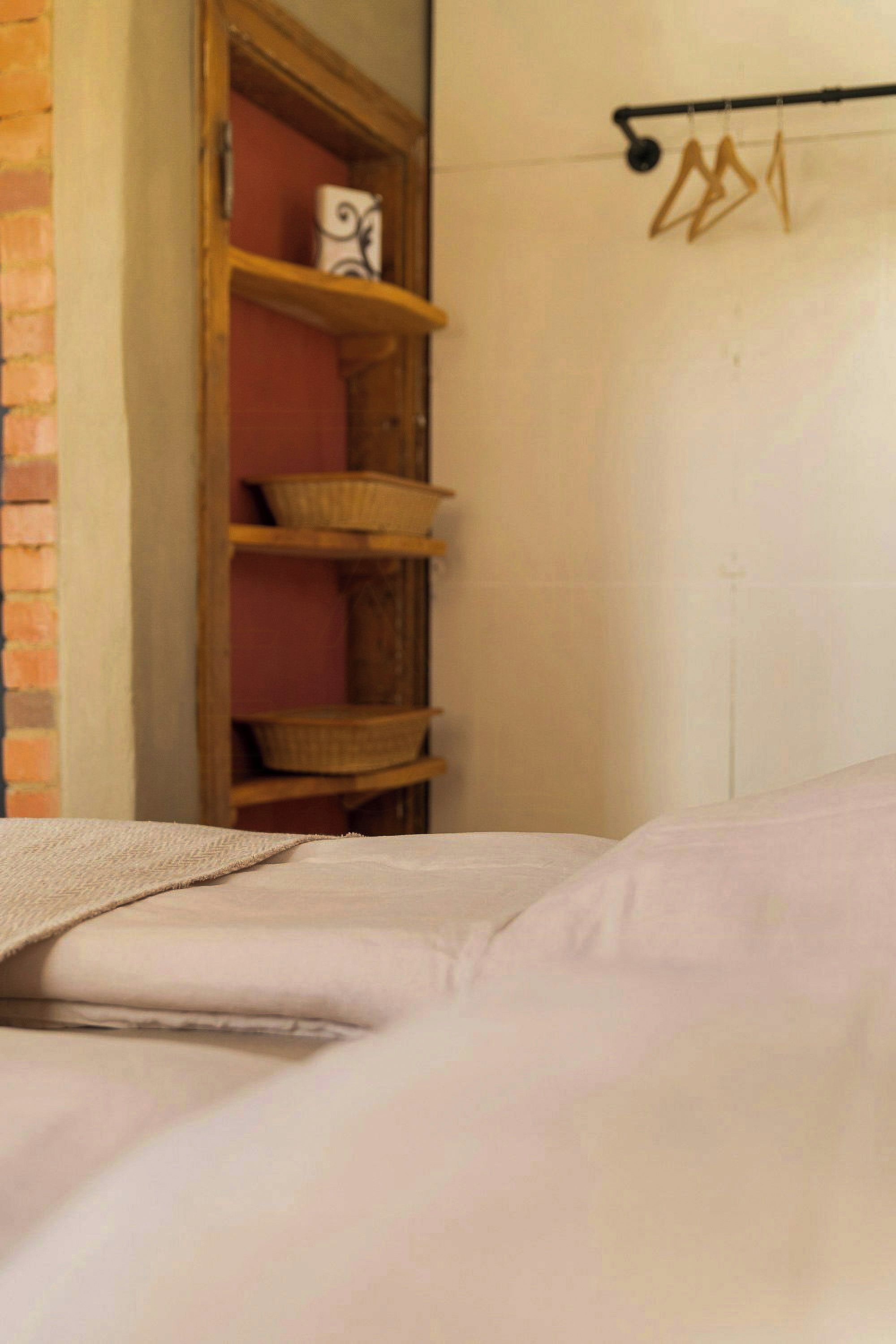 Een slaapkamer met een bed, een houten plankenwand met manden, en een wandrek met kledinghangers.