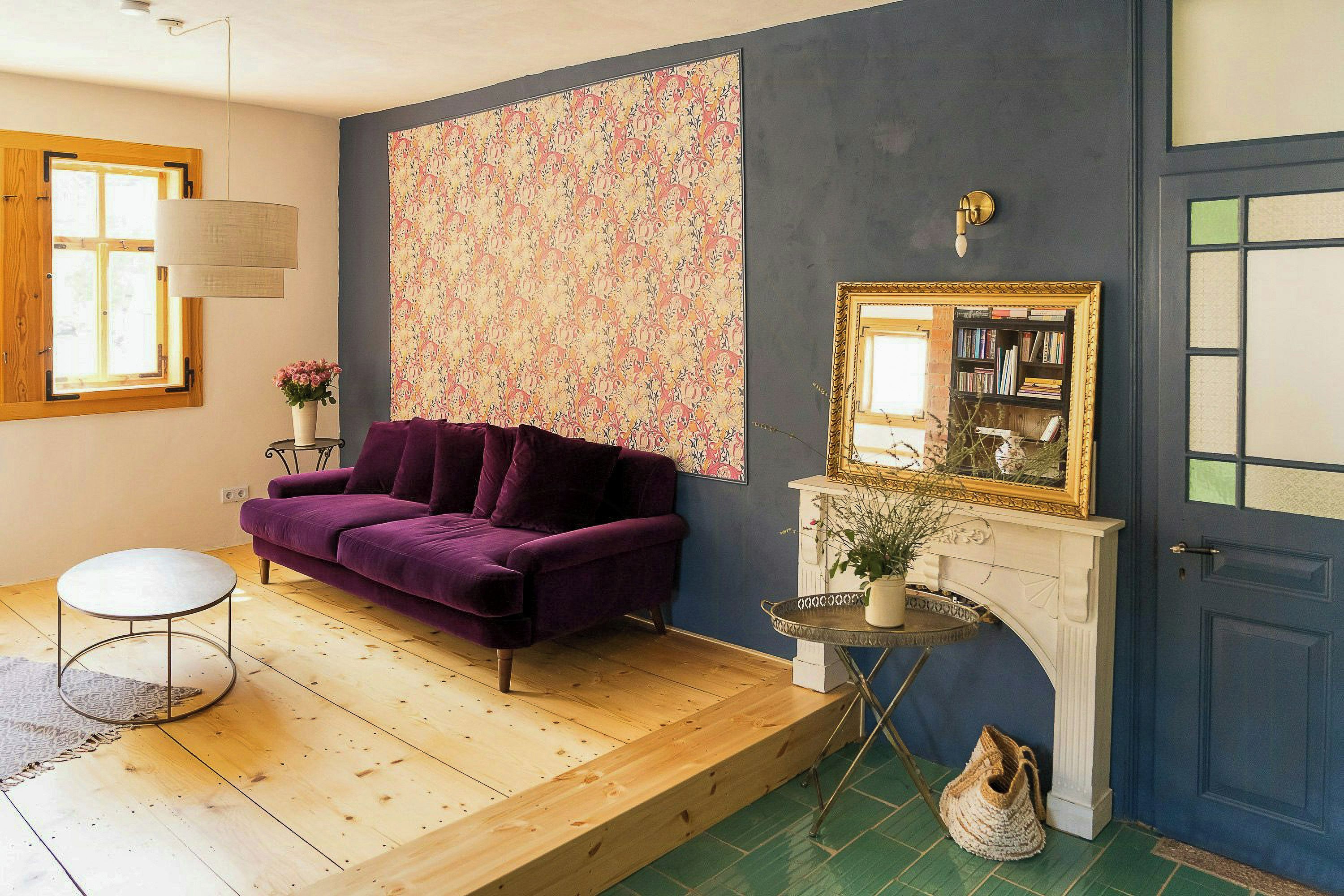 Een kamer met een paarse bank, een klein rond tafeltje, een open haard met spiegel en een kamer met een patroon.