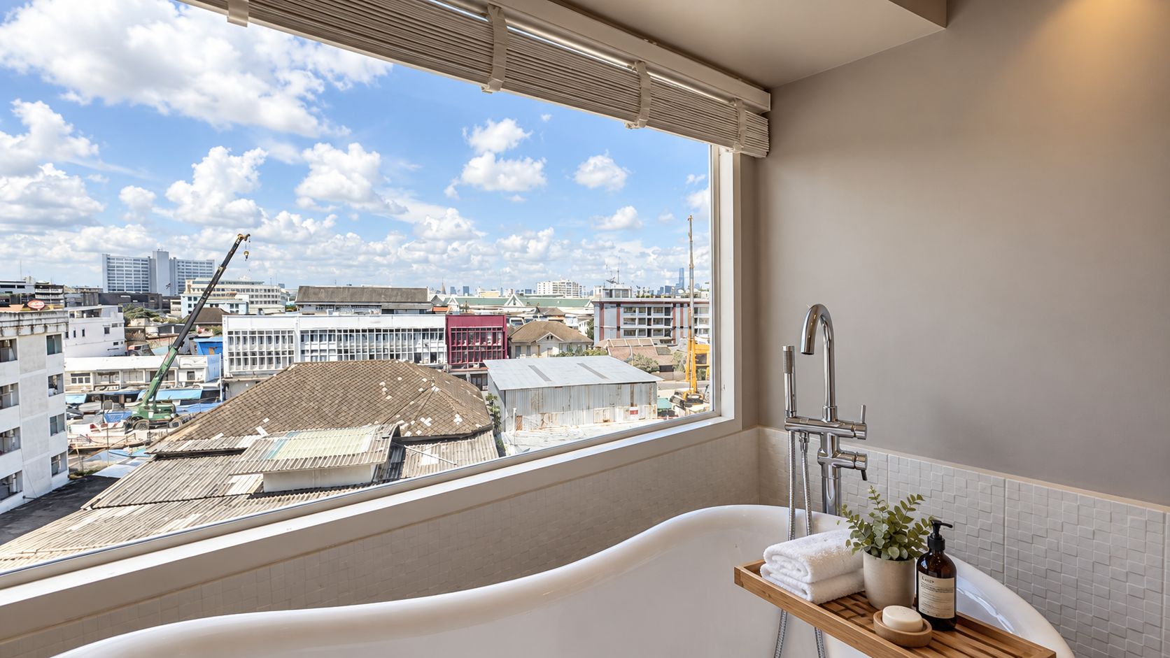 Ein modernes Badezimmer mit einer freistehenden Badewanne, einem Fenster mit Blick auf die Stadt und einer kleinen Holztrennwand für Toilettenartikel.