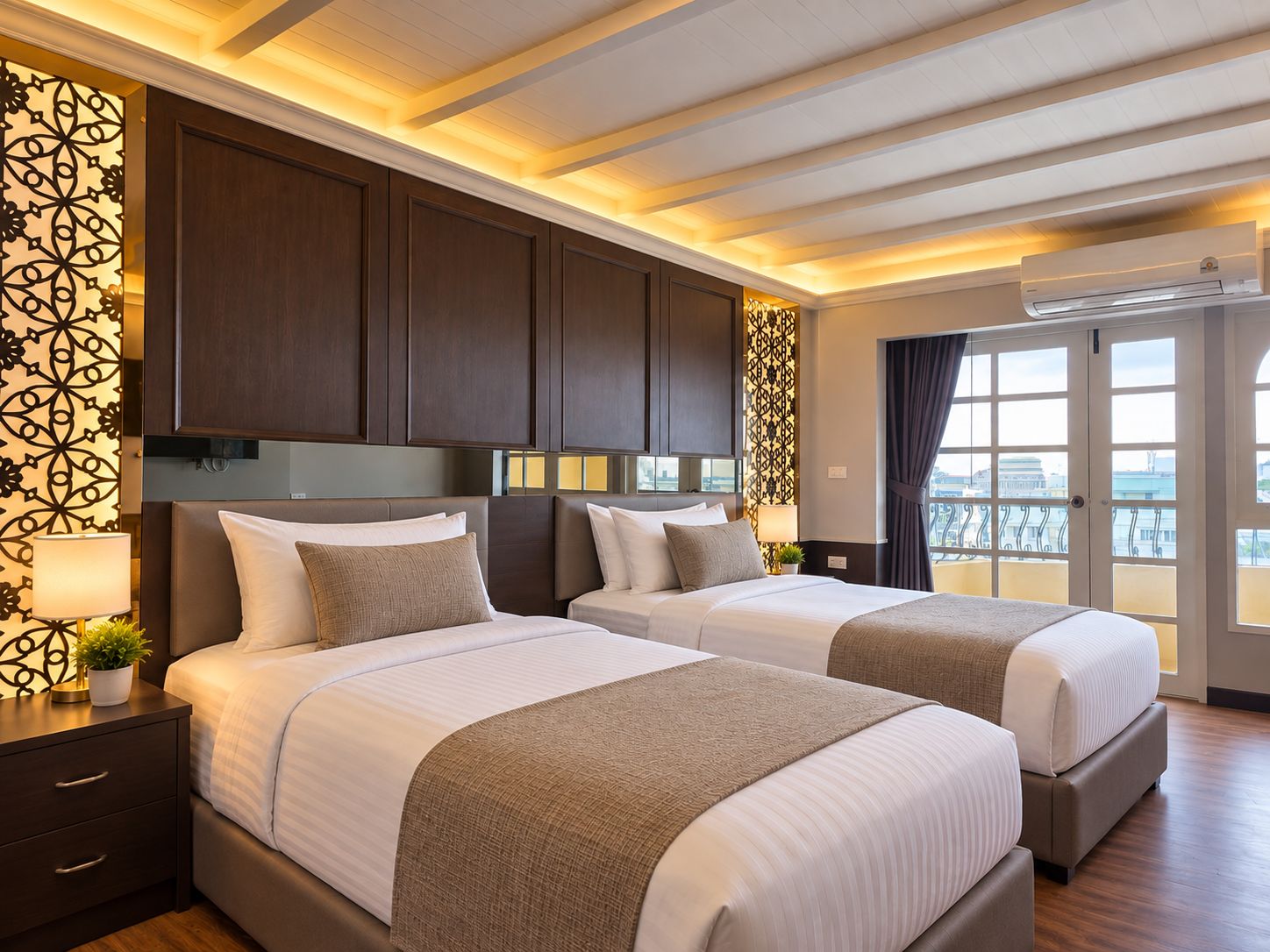 Ein Hotelzimmer mit zwei Betten, dunklen Holzvertäfelungen, einem Balkon mit Blick und einer Klimaanlage.