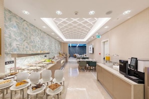 Un comedor moderno de hotel con bufé, asientos y un techo con diseño geométrico.