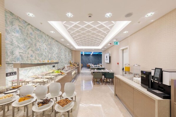 Un comedor moderno de hotel con bufé, asientos y un techo con diseño geométrico.