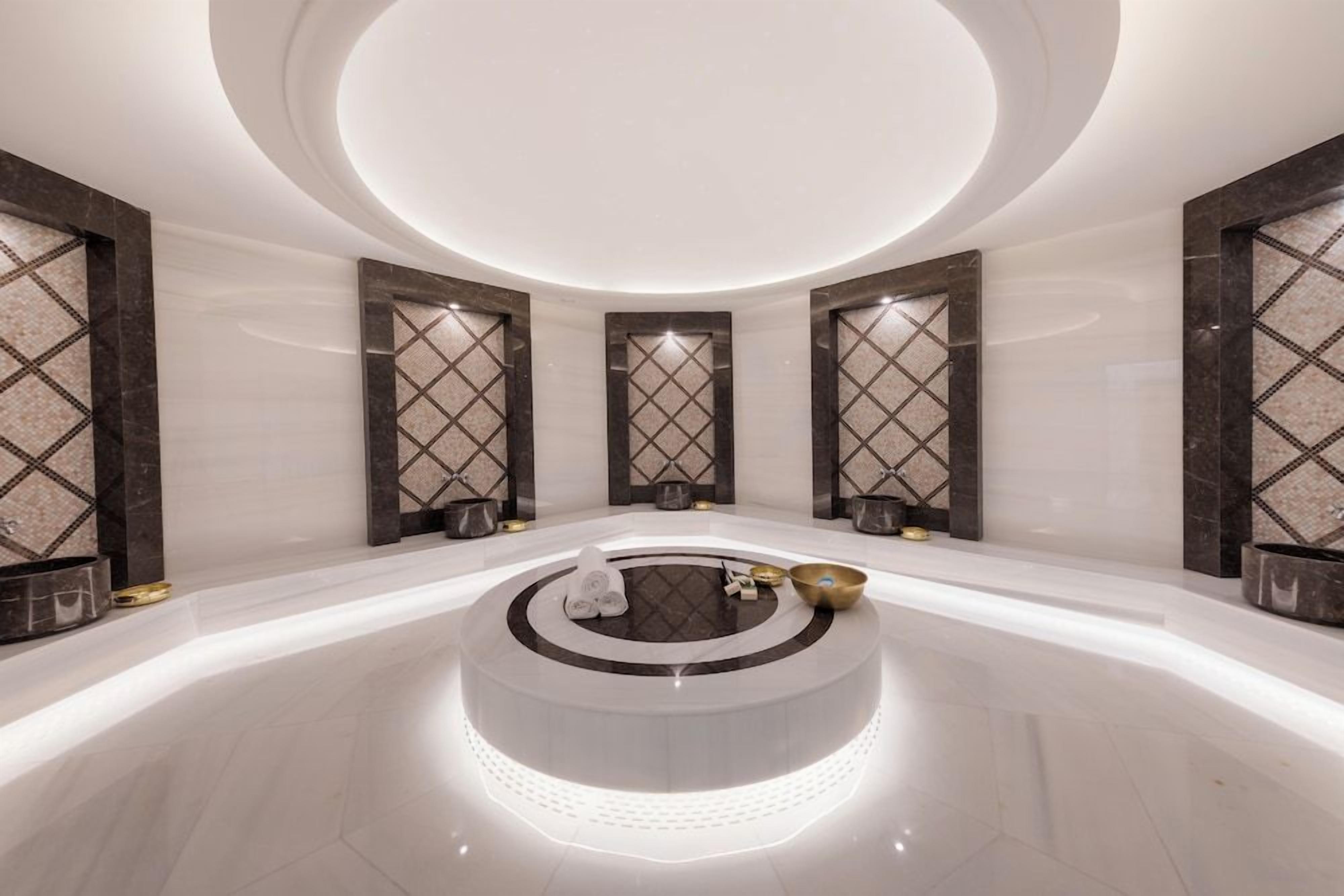 A modern spa area with a central circular platform, marble flooring, and wall-mounted decorative panels.