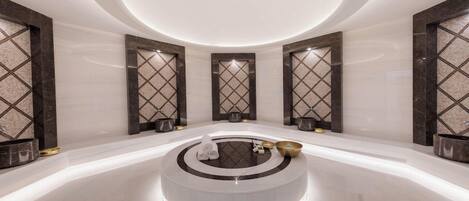 A modern spa area with a central circular platform, marble flooring, and wall-mounted decorative panels.
