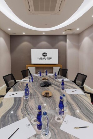 Un salón de conferencias con una mesa de mármol, sillas, botellas de agua y una pantalla que muestra el nombre del hotel.