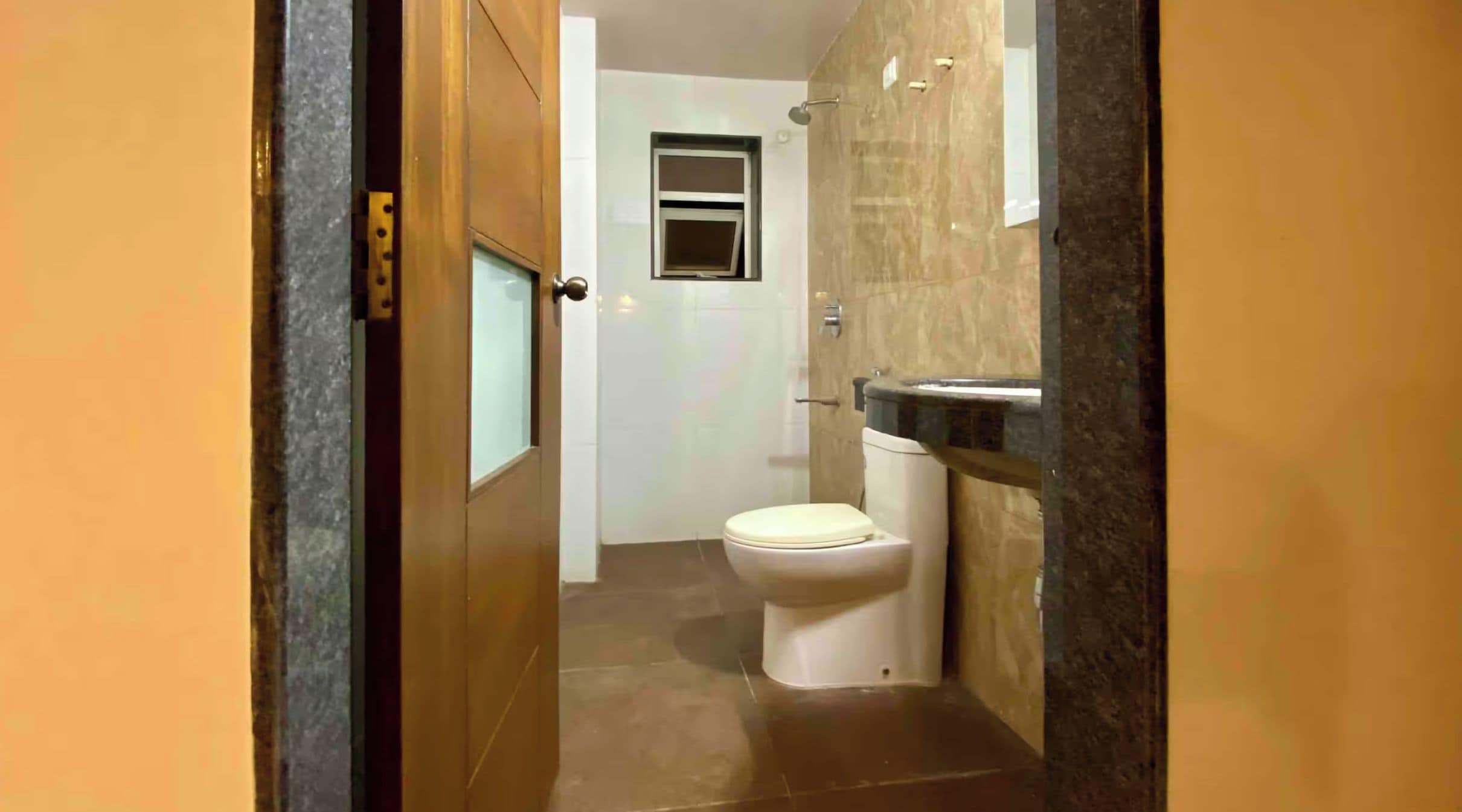 Un couloir étroit mène à une salle de bain équipée de toilettes et d’un espace douche.