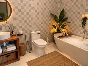 Ein Badezimmer mit weißem Waschbecken, WC und Badewanne. Auf den Ablagen befinden sich Pflanzen und Pflegeprodukte.