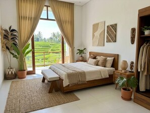 Ein Schlafzimmer mit einem großen Bett, einem Nachttisch, einer Bank, einer Topfpflanze und Blick auf eine grüne Landschaft durch ein Fenster.
