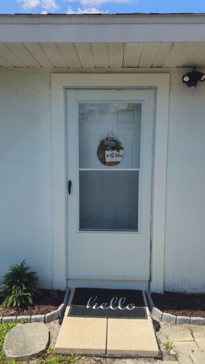 Una porta d'entrada amb un rètol de 'welcome', un estri de peu amb la paraula 'hello' i una petita planta al costat.