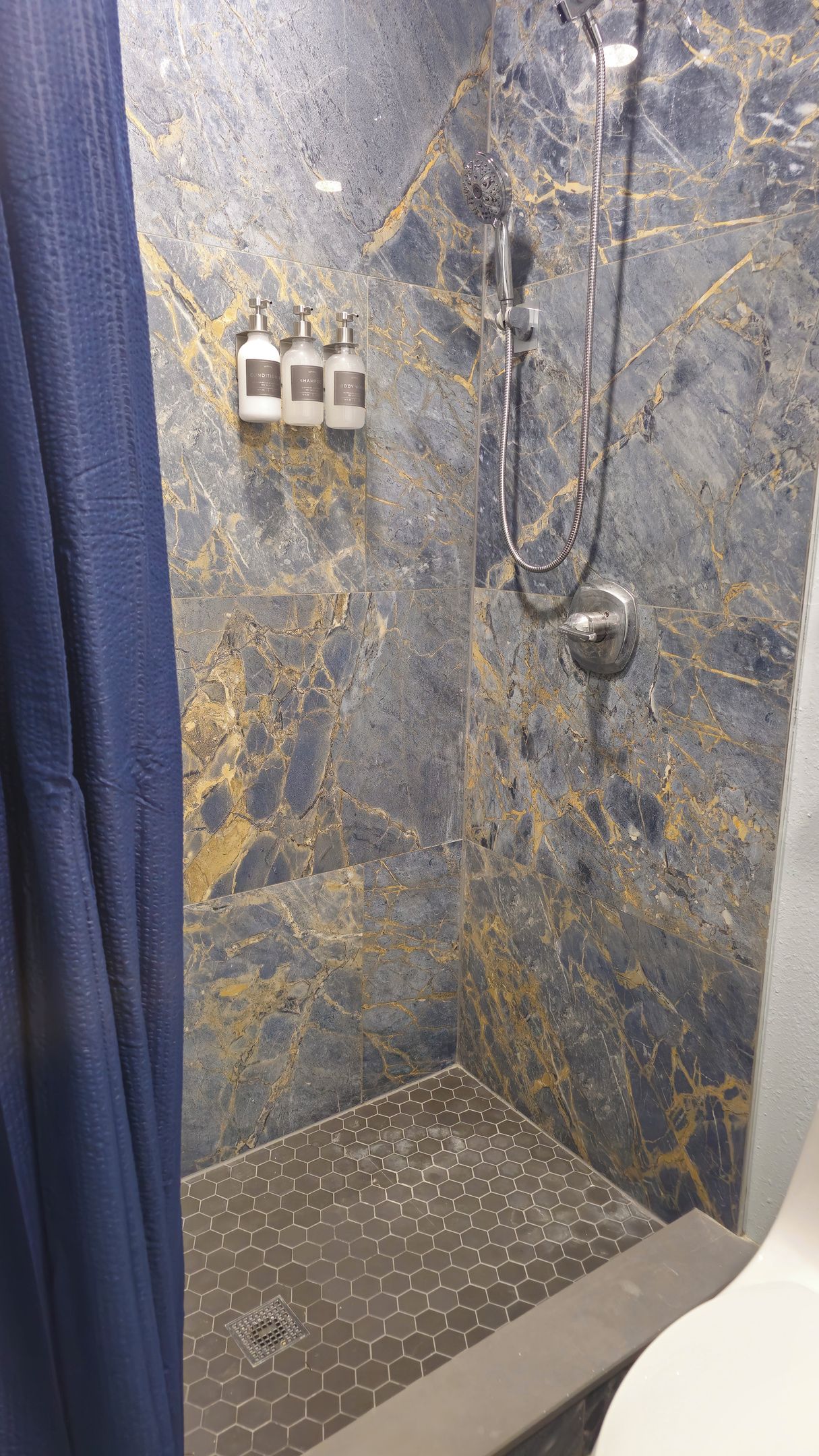 A shower area with a marble wall, a showerhead, and two bottles of shampoo.