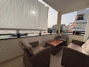 A balcony with wicker furniture, a table, and a view of buildings in the distance. - LOS JUNCOS I APARTMENT (401) (San Bartolomé de Tirajana)
