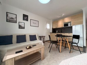 A modern living space with a sofa, coffee table, and dining area. - LOS JUNCOS I APARTMENT (401) (San Bartolomé de Tirajana)