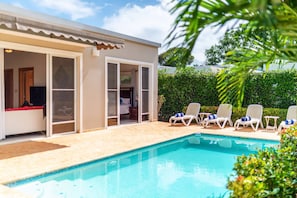 A swimming pool with lounge chairs, a covered patio, and a bedroom with a TV. - Casa Linda ll Villa 925 (Sosúa)