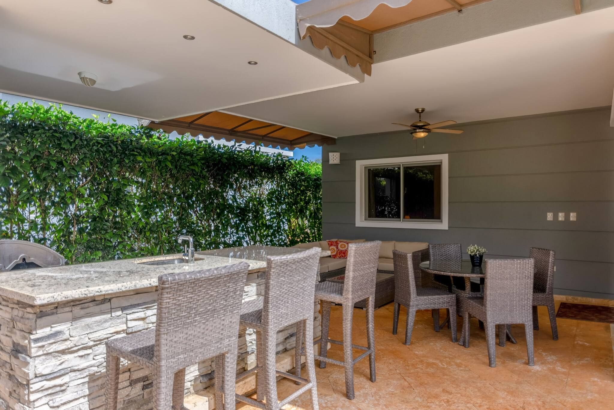 Une terrasse extérieure avec un bar en pierre, des fauteuils en osier et un ventilateur de plafond.