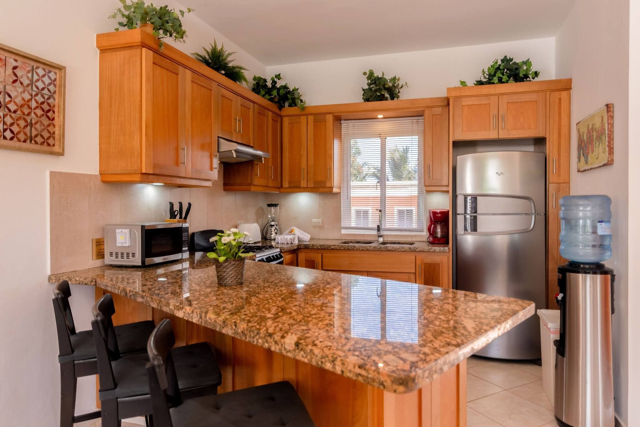 A kitchen with wooden cabinets, a granite countertop, a stainless steel refrigerator, and a water dispenser.