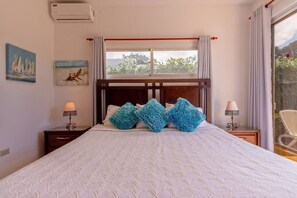 Een slaapkamer met een bed, twee nachtkastjes, een raam met gordijnen en kunst aan de wanden.