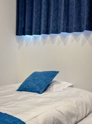 Ein Bett mit weißer Bettwäsche und einem blauen Kissen, ein dunkelblauer Vorhang und eine weiße Wand.
