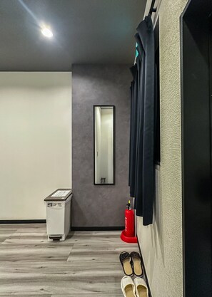Ein Hotelzimmer mit Holzboden, einer weißen Mülltonne, einem roten Feuerlöscher, einem Spiegel und einem Paar Schuhe.